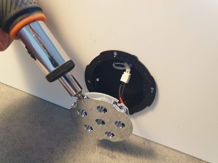 Närbild på en person som installerar en LED-spot i ett skåpsuttag med hjälp av en skruvmejsel, exponerade kablar synliga.