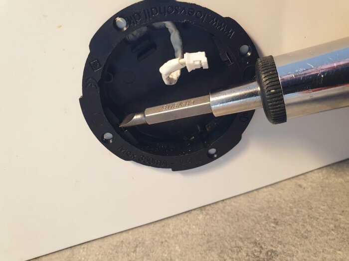 Inskruvning av en LED-spott med en skruvmejsel i en svart monteringsring, med fokus på installationsförfarandet för eluttag.