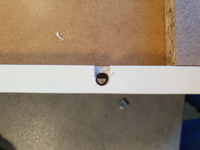 Hål för LED-spot med avsliten yta på en skåplucka, visande en del av en arbetsyta vid byte av möbelspotar.