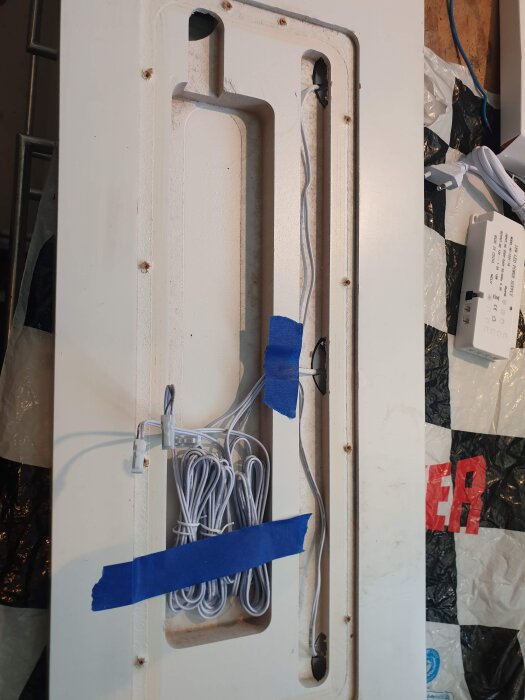 Bild av baksidan av ett skåp med monterade kablar och blå tejp. Två LED-drivdon och kablar är fästa på panelen för spotbelysning.