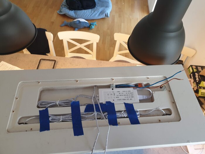 LED-drivdon monterat i ett skåp med kablar fastsatta med blå tejp; omgivning visar köksmiljö med stolar och belysning ovanför.