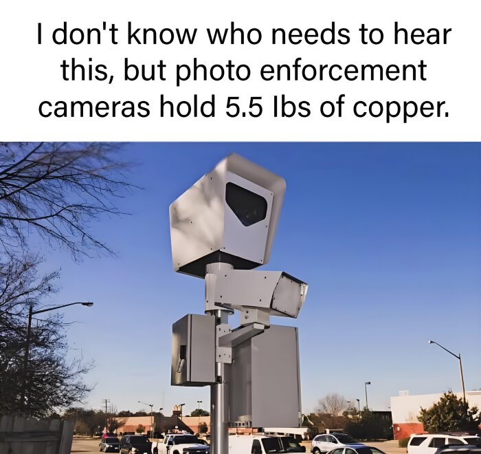 Övervakningskamera på stolpe vid parkering med bilar i bakgrunden, mot en klarblå himmel. Text om kopparinnehåll i kameran.