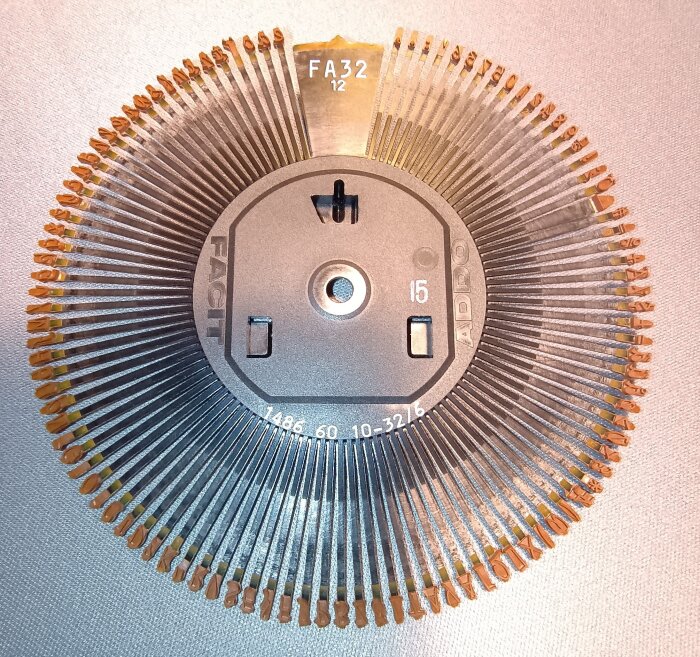 Typkula från äldre skrivmaskin, märkt "FA32 12" med text kring kant, använd i tidiga IBM-maskiner.