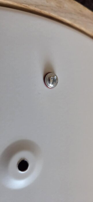 Närbild av skruv som sticker ut 3 mm från lampans metallram, monterad på ovansidan mot gipstaket.