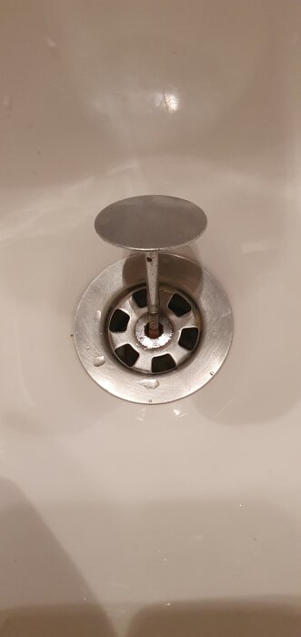 Närbild av ett handfat med en sil i metall och en upphöjd pop up-propp ovanför silen.