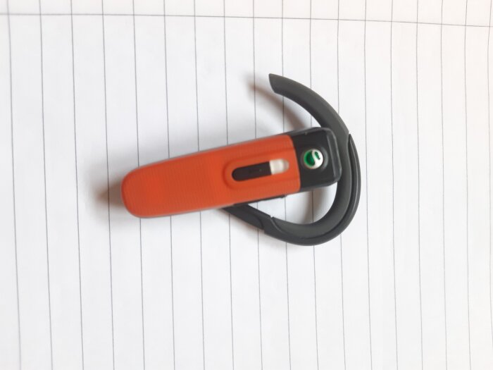Ett Bluetooth-headset med orange och svart design ligger på ett randigt papper.
