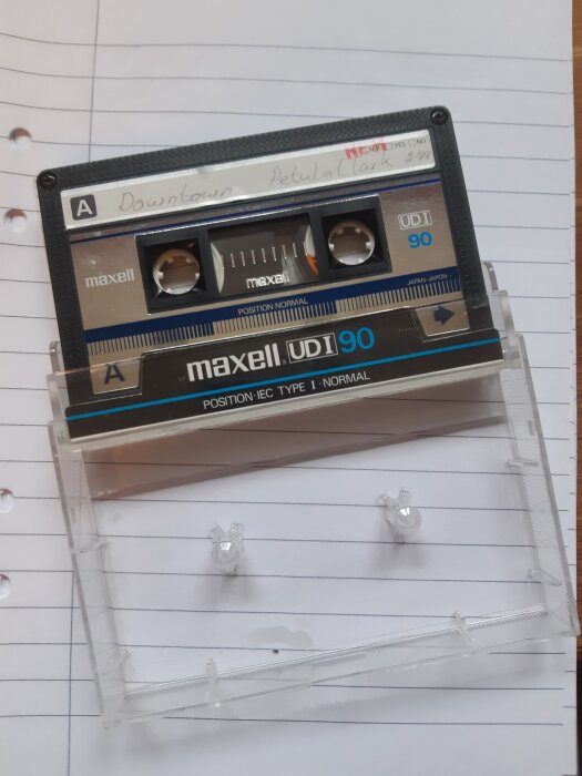 Kassettband av märket Maxell UD 90 med etikett som säger "Downtown Petula Clark", liggande på linjerat papper.