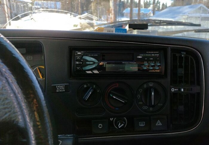 Instrumentbräda i bil med en Alpine bilstereo, ratt och ventilationsreglage synliga. Uppgradering med 3.5mm-anslutning nämns i texten.