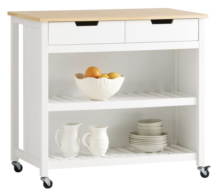 Köksmöbel med trähylla och två lådor, skål med frukt, staplade tallrikar och kannor under. Möbeln har hjul för enkel förflyttning.