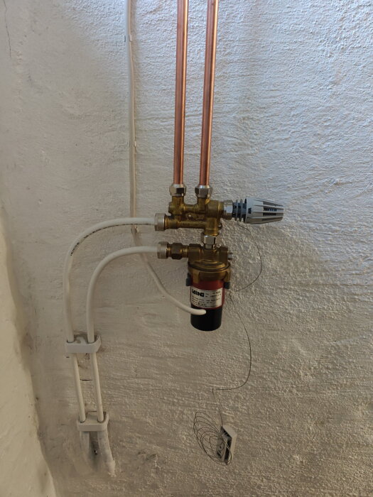Shunt monterad på golvvärmerör med kopparrör, vit termostat och ledningar mot en vit vägg, saknar cirkulation.