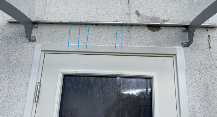 Fasad med synliga fuktränder ovanför en dörr, markerat med blå linjer som indikerar vattenläckage från taket över entrén.