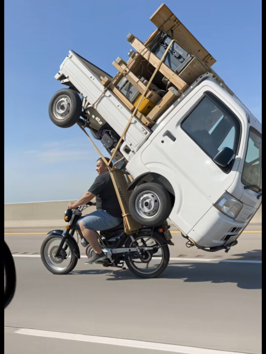 Man kör en moped med en skåpbil och träkonstruktioner fastsurrade på ryggen.