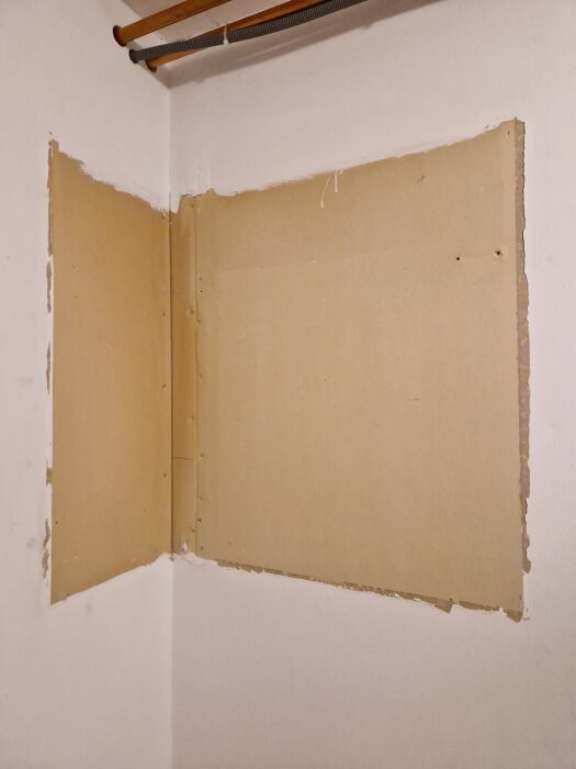 Vägg med spår efter borttagna spikar i ett skåp, synliga skruvhål och ett rör i ovankant.