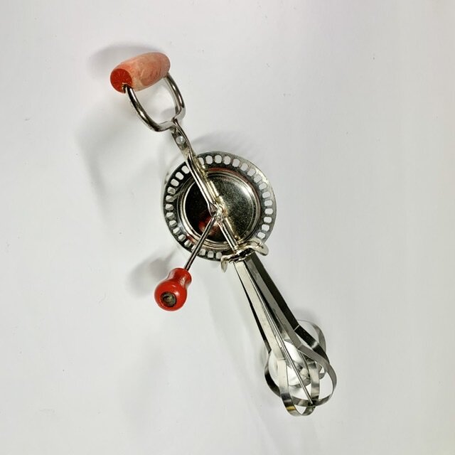 Handvisp i metall med rött trähandtag, brukad köksredskap från 1950-talet.