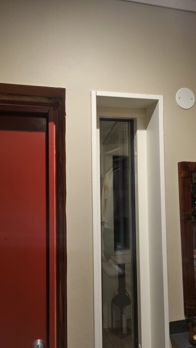Dörrkarm med röd dörr bredvid en smyglist och fönsternisch; fråga om att montera smygar mot karmen.