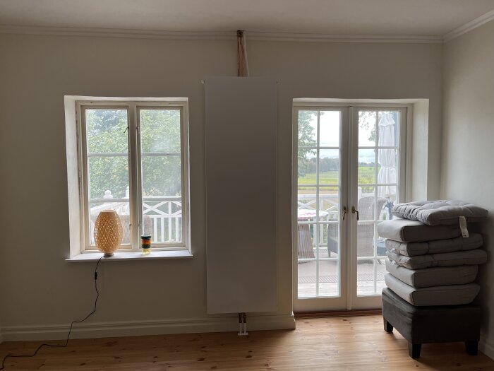 Vitt element monterat vertikalt mellan två fönster, med en lampa och ett ljus i vänstra fönsternischen, samt dynor staplade till höger.