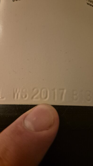 Närbild på en präglad text "WS 2017" på en slät yta med ett finger som pekar mot texten.