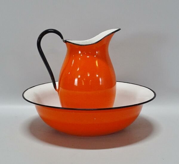 Orange kanna och fat av emalj med svart kant mot ljus bakgrund.