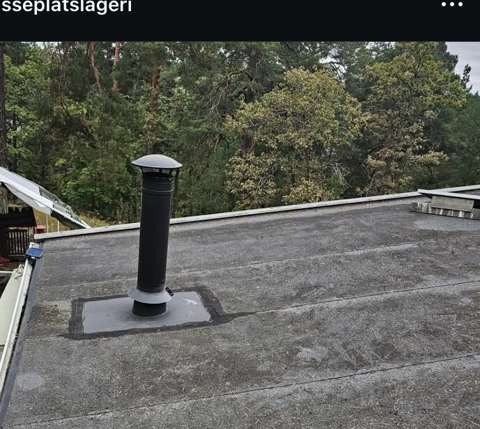Platt tak med svart skorsten utan regnkrage, omgiven av skog. Tätning verkar vara otillräcklig, vilket orsakar läckage.