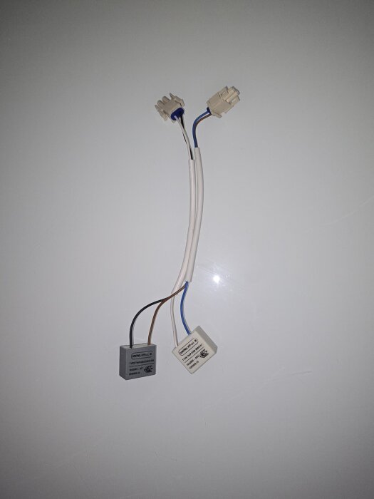 Två beige och vita elkablar med anslutningar ligger på ett vitt underlag, relaterade till problem med en Electrolux frys som inte kyler.