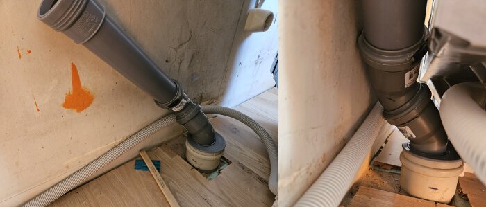 Grått avloppsrör anslutet nära golvet, omgivet av trä och en vägg med orange fläck, samt vit slang i närheten.