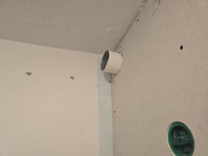 Ventilationsrör och uttag i ett hörn, med dragna kablar för CAT6, synliga skruvhål och ett grönt kabelutlopp på en gipsvägg.