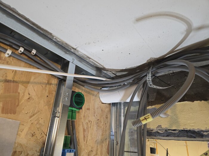 Ventilationsrör, flexrör och elektriska installationer i ett rum under renovering med synlig isolering och OSB-skiva.