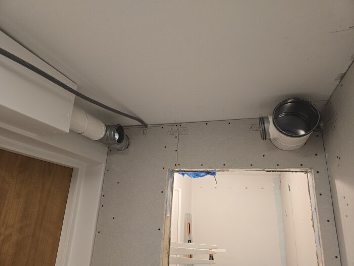 Klädkammare med synligt spirorörsventilationssystem monterat i taket, bredvid en dörröppning. Väggarna är oskivade.