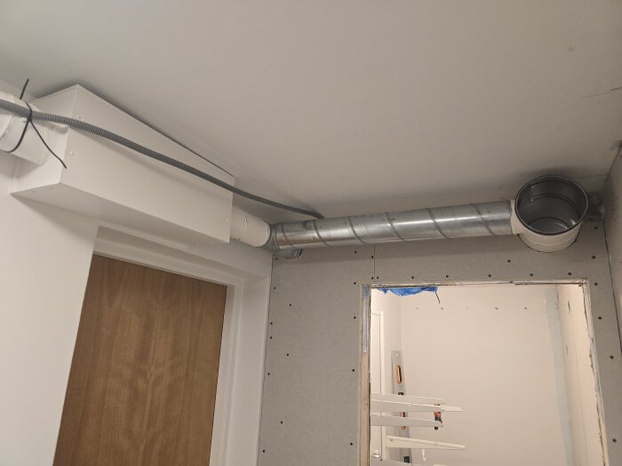 Ventilationsrör monterade i ett rum med synliga gipsväggar och flexrör för nätverkskablar bredvid. Dörr och öppning i väggen syns.