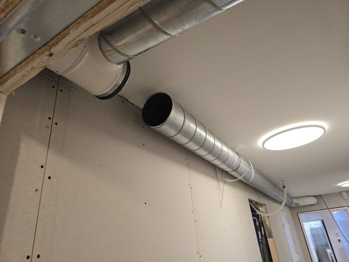 Ventilationsrör monterade i taket, inklusive en rund lampa och en dörröppning i bakgrunden, under renovering.