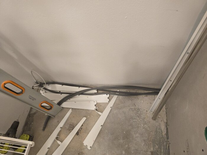 CAT6 flexrör för nätverk, placerade på betonggolv bredvid vit vägg, med nivåmätare och byggmaterial synligt.