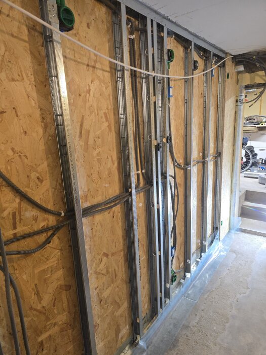 Byggvägg med monterad kabeldragning och ventilationsrör i källarprojekt, före isolering och OSB-skivor. Verticala flexrör för CAT6 syns.