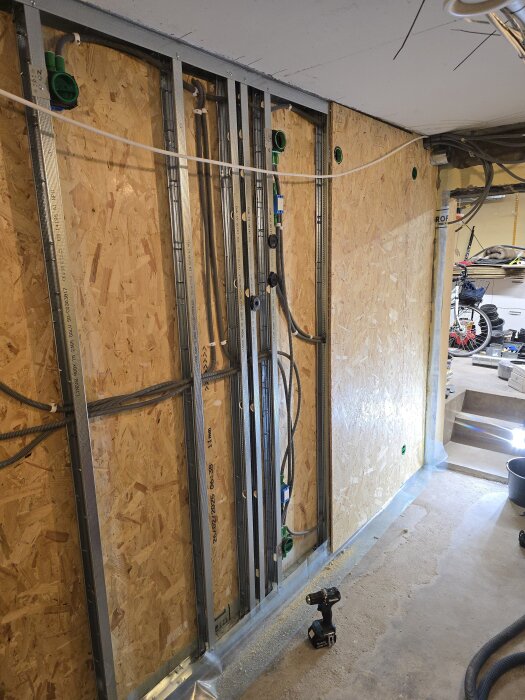 Vägg av OSB med synliga flexrör för CAT6 och ventilationssystem. Verktyg på golvet; förberedelser för ventiler och nätverk i källarprojekt.