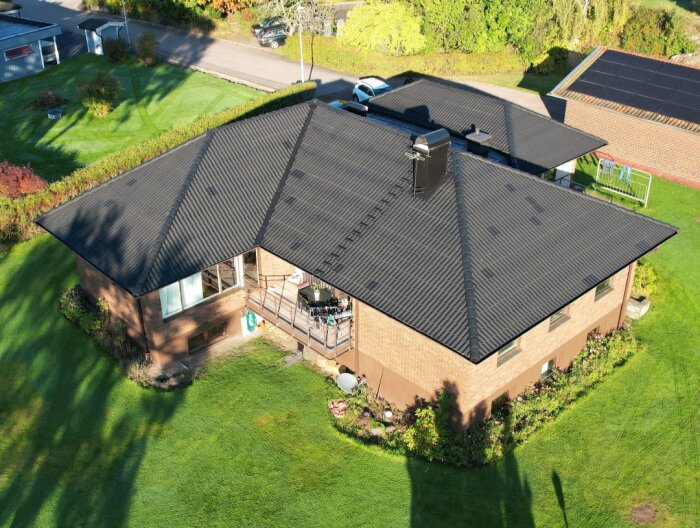 Svartmålat tak på en tegelvilla med grönskande trädgård, fotograferat från ovan i dagsljus.