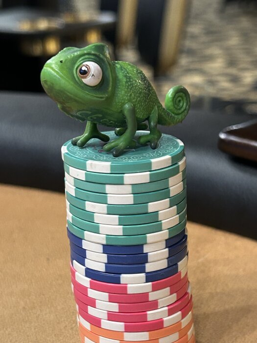 Grön kameleontfigur står på en stapel av färgglada pokermarker på ett bord.
