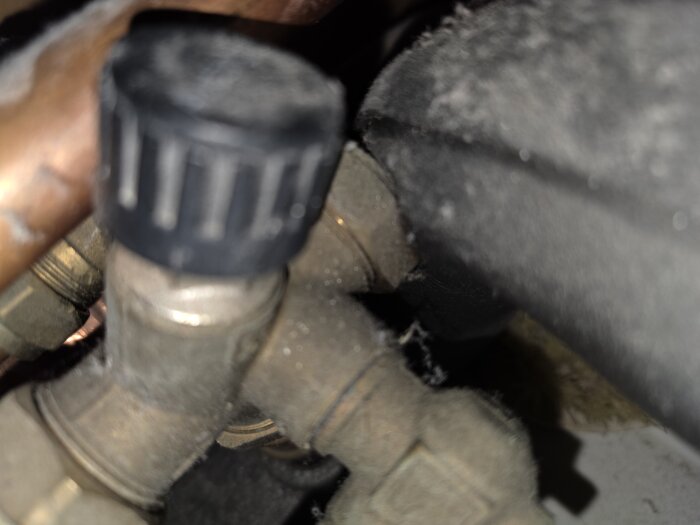 Ventil med svart vred och rör i ett värmesystem, eventuell påfyllningspunktsventil för NIBE F1245, närbild för hjälp med korrekt identifiering.