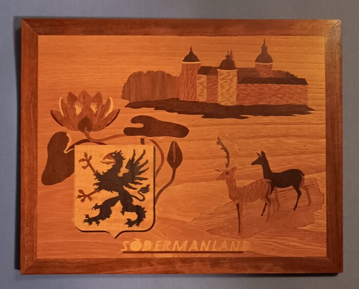 Intarsia med Södermanlands landskap innehållande ett slott, två rådjur, en vapensköld med en grip och en blomma.