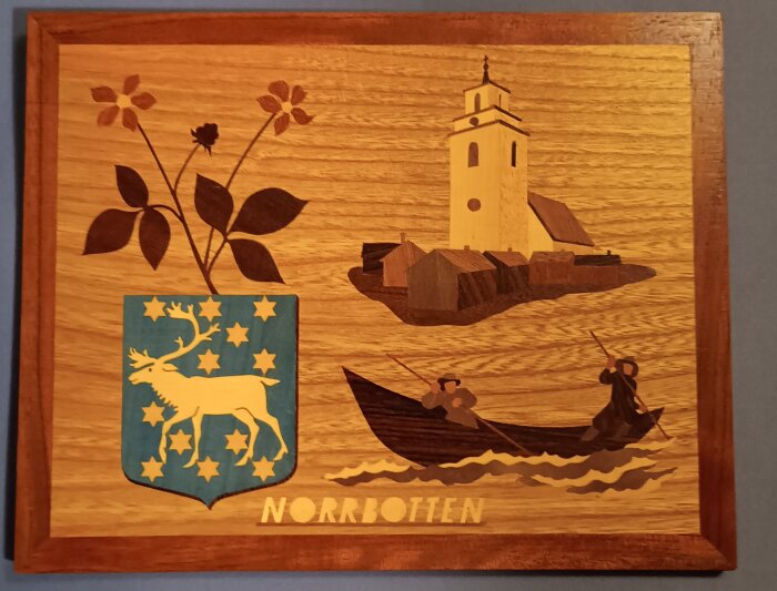 Träintarsia med ett blomstermotiv, en kyrka, en båt med två roddare, och ett vapen med en älg. Texten "Norrbotten" syns längst ner.