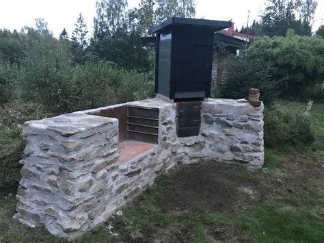 Utomhusgrill av sten med en metallhuv i en trädgårdsmiljö.