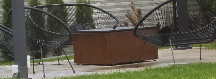 Två stolar och en trälåda står på en uteplats med grönt gräs och trappsteg i bakgrunden.