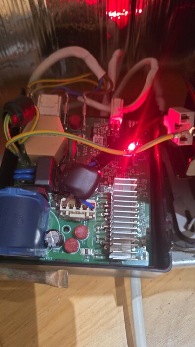 Kretskort med röd diod som lyser, omgiven av kablar och komponenter, relaterat till Electrolux frysmodellen EUE9000X.