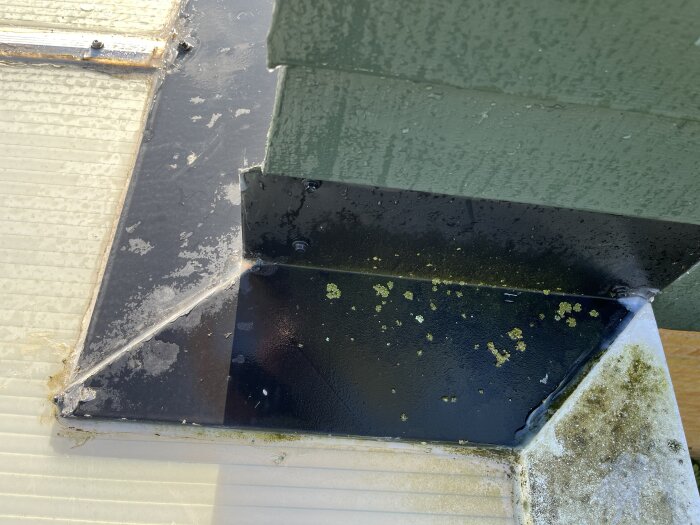 Hörn av tak med plåtskarv och grön panel, där silikon används för tätning, men fukt och droppar synliga.