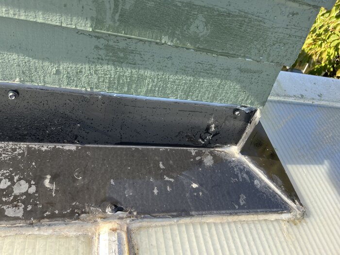 Hörn vid tillbyggnad med fuktspår på svart plåt och silikon. Grön panelvägg ovanför. Foto visar område där läckage uppstår vid regn.