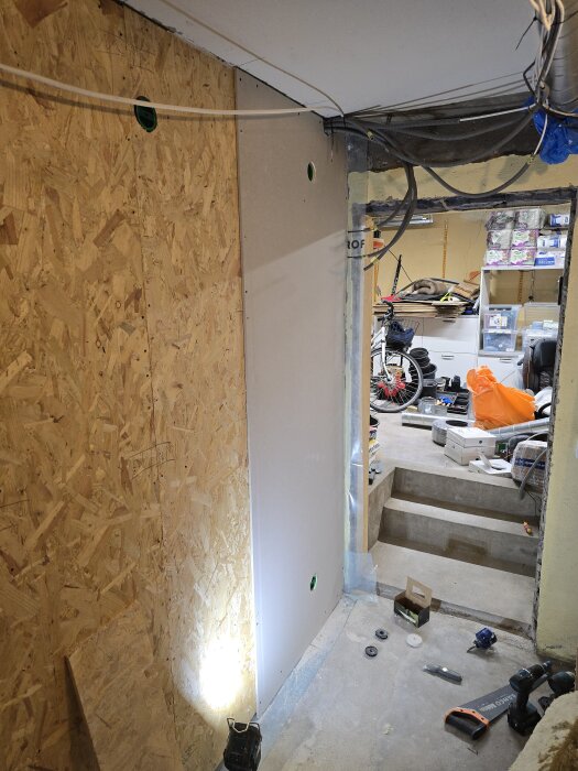 OSB-skivor och gipsskivor på en vägg under byggnation i ett hobbyrum, med verktyg och material spridda över golvet.