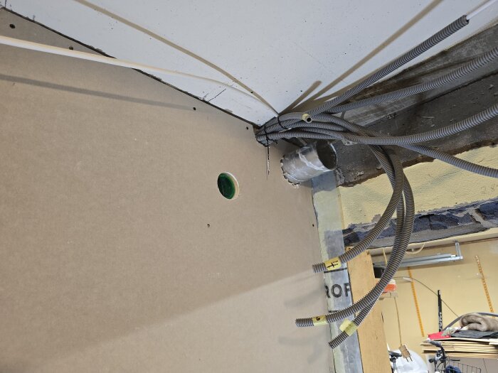 Rör och kablage för ventilation och el installation i ett rum under renovering, med hål för spirorör och synlig isolering i väggen.
