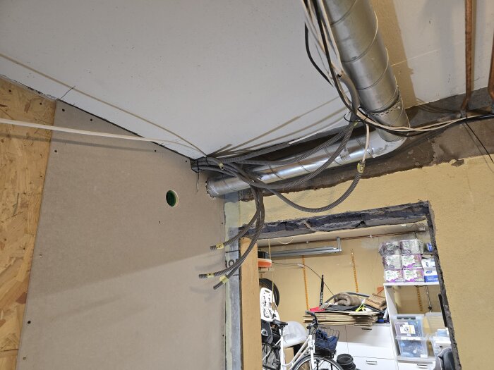 OSB-skiva och gipsskiva mot tak med ventilationsrör och kablar i ett rum under renovering. Hål för spiralrör syns också.