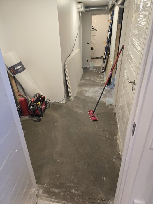 En nymålad korridor med gipsskivor som står lutade mot väggen, en mopp och verktyg. Dörr in till ett rum i slutet av korridoren.