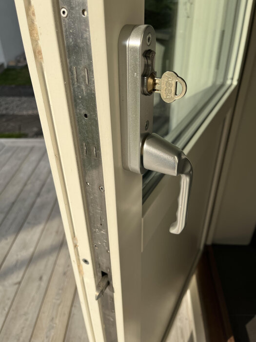Dörr med ett metallhandtag och ett nyckelhål med en nyckel märkt "ASSA" isatt, sedd från insidan mot en öppen veranda.