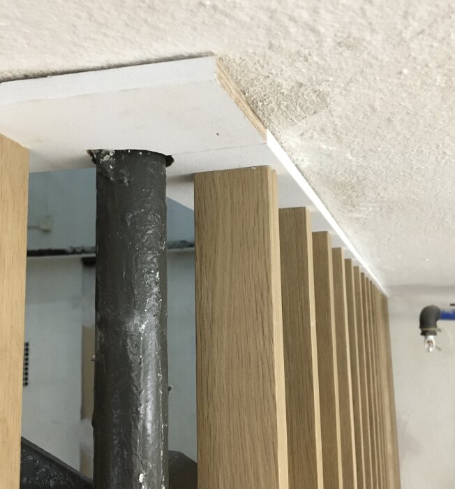 Spaljé med träpinnar och plyfa monterad i tak, med ett svart järnrör inskjutet genom plyfan.