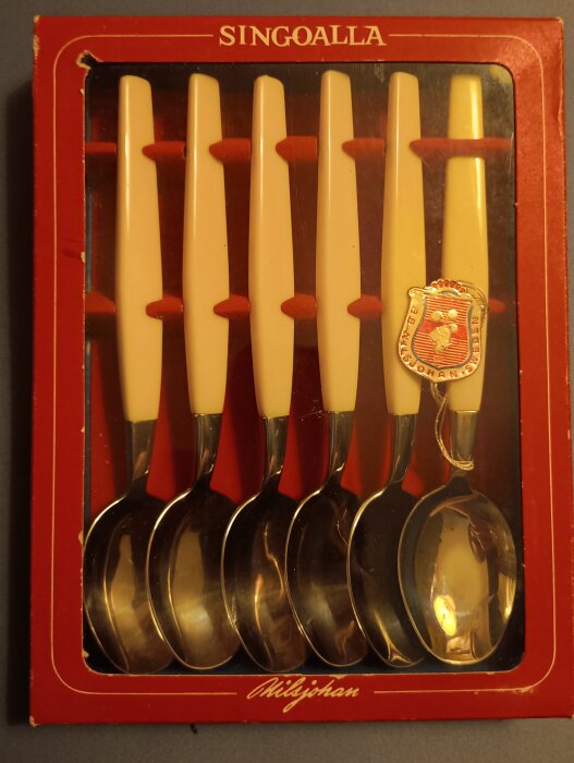 Sex Nilsjohan Singoalla skedar i förpackning med vita handtag och rostfritt stål, designade i färgglad plast av kända designers.